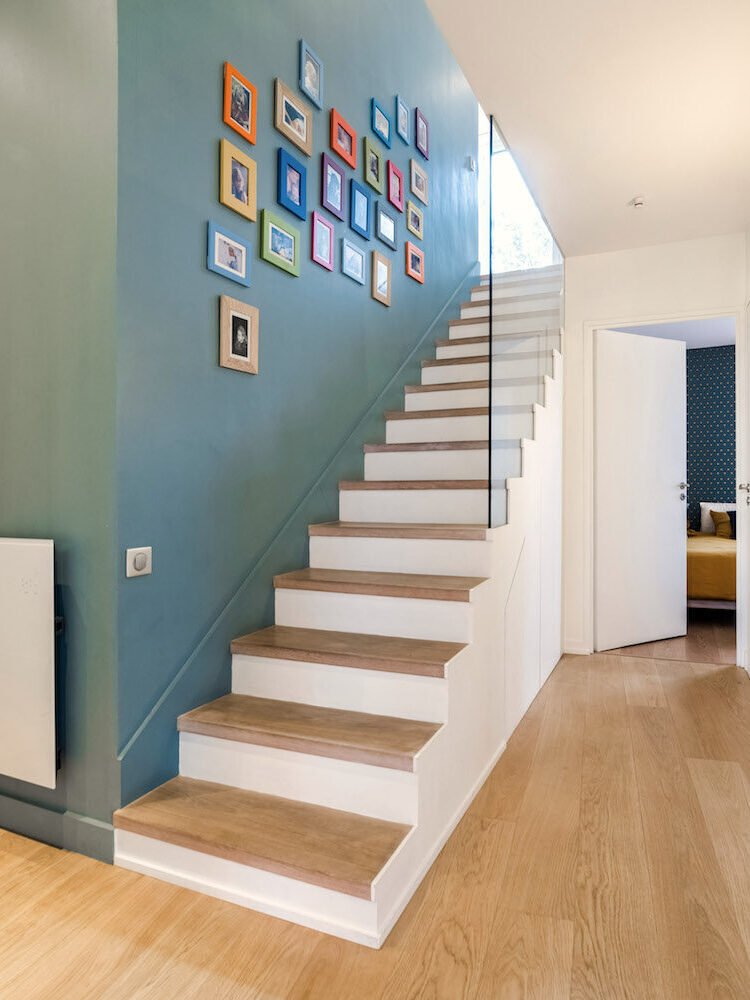 Escalier blanc et bois, mur bleu orné de cadres colorés – duplex rénové Vincennes