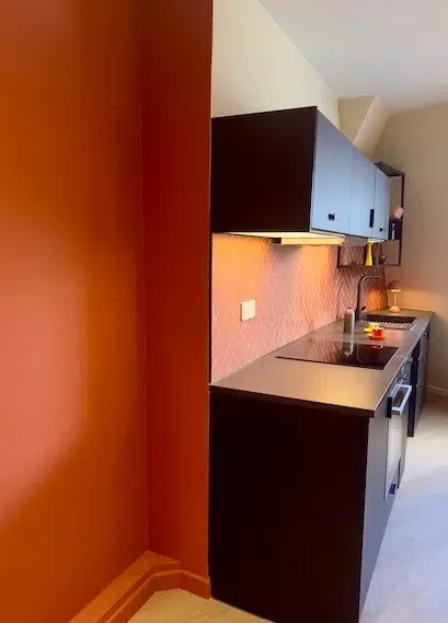 Cuisine linéaire noire sous combles et mur terracotta – appartement rénové Boulogne-Billancourt