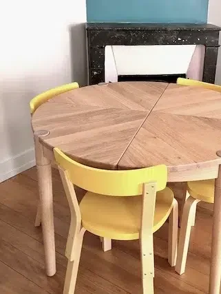 Aménagement d'un studio de 25m² - Paris 10 4 Salle à manger avec Table ronde en bois et chaises jaunes devant la cheminée – studio Soleil aménagé Paris 10