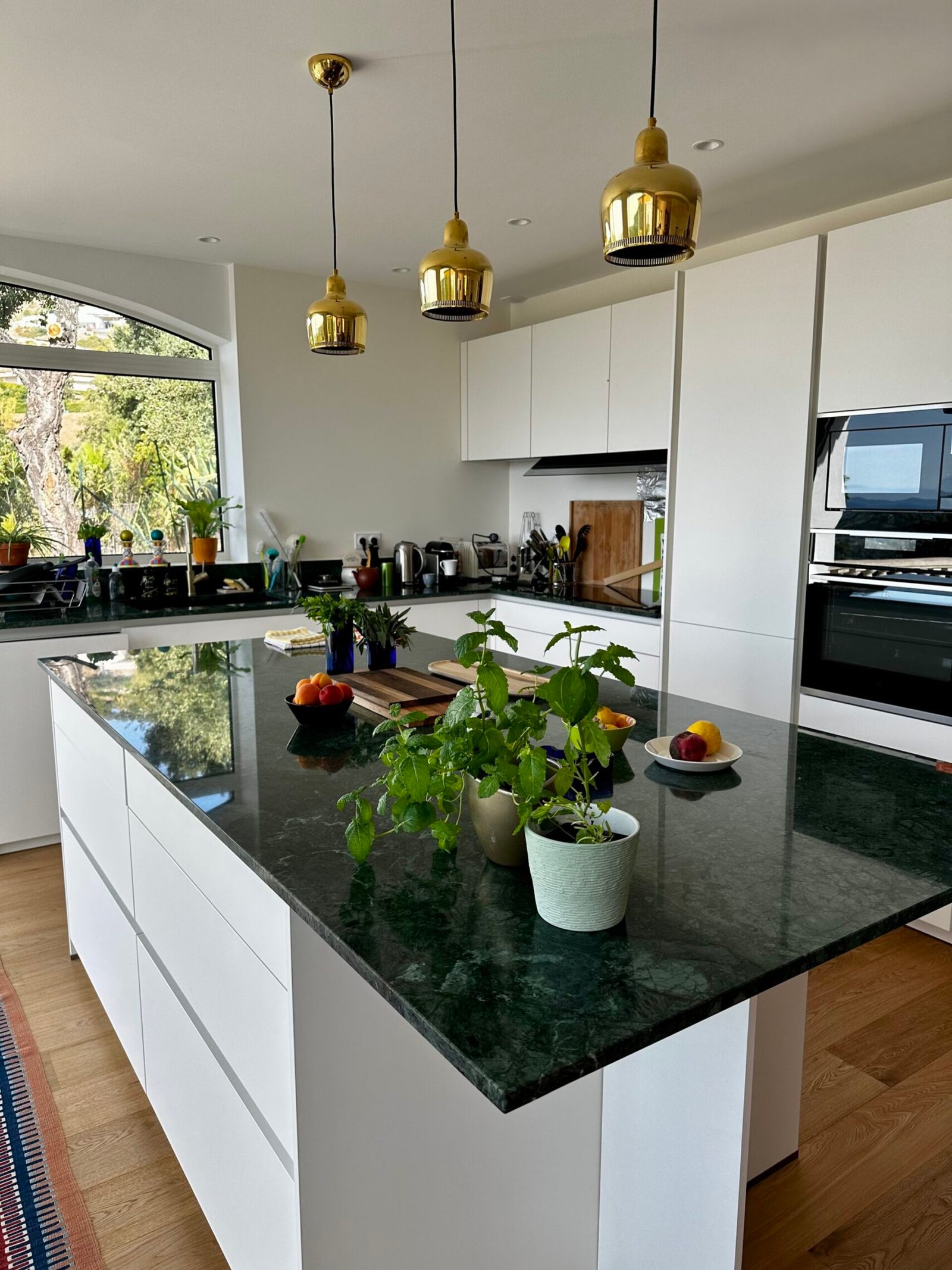 Cuisine blanche laquée avec îlot en marbre vert et suspensions dorées après rénovation – maison à Hyères