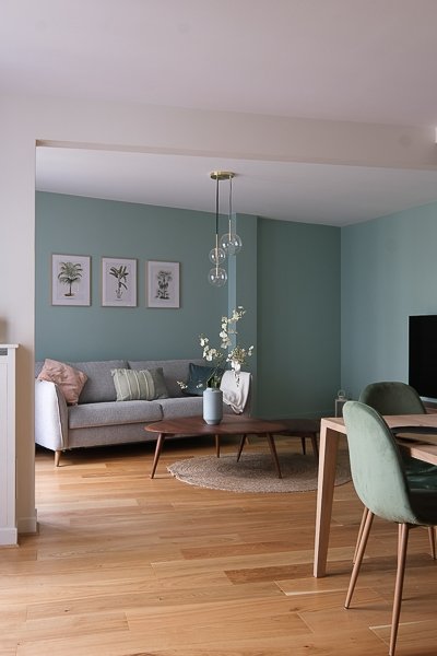 Salon vert céladon avec canapé gris et parquet en chêne clair – appartement rénové Paris 9