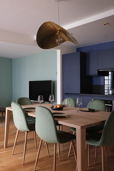 Salle à manger avec table en bois, chaises vert sauge et luminaire dorée – appartement Paris 9