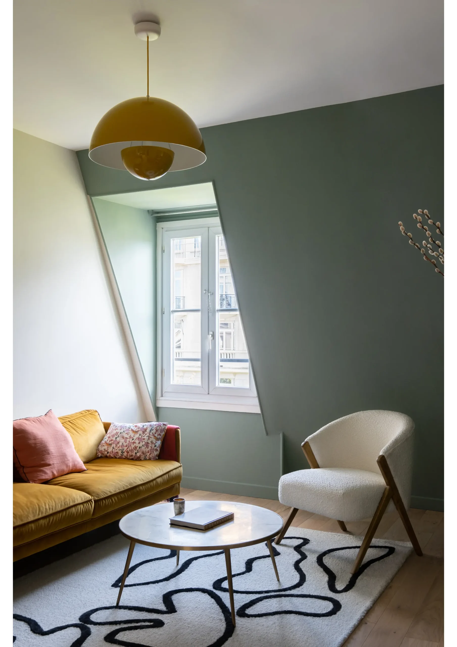 Salon mansardé vert sauge avec canapé et suspension jaunes et tapis graphique – appartement sous combles Paris 17