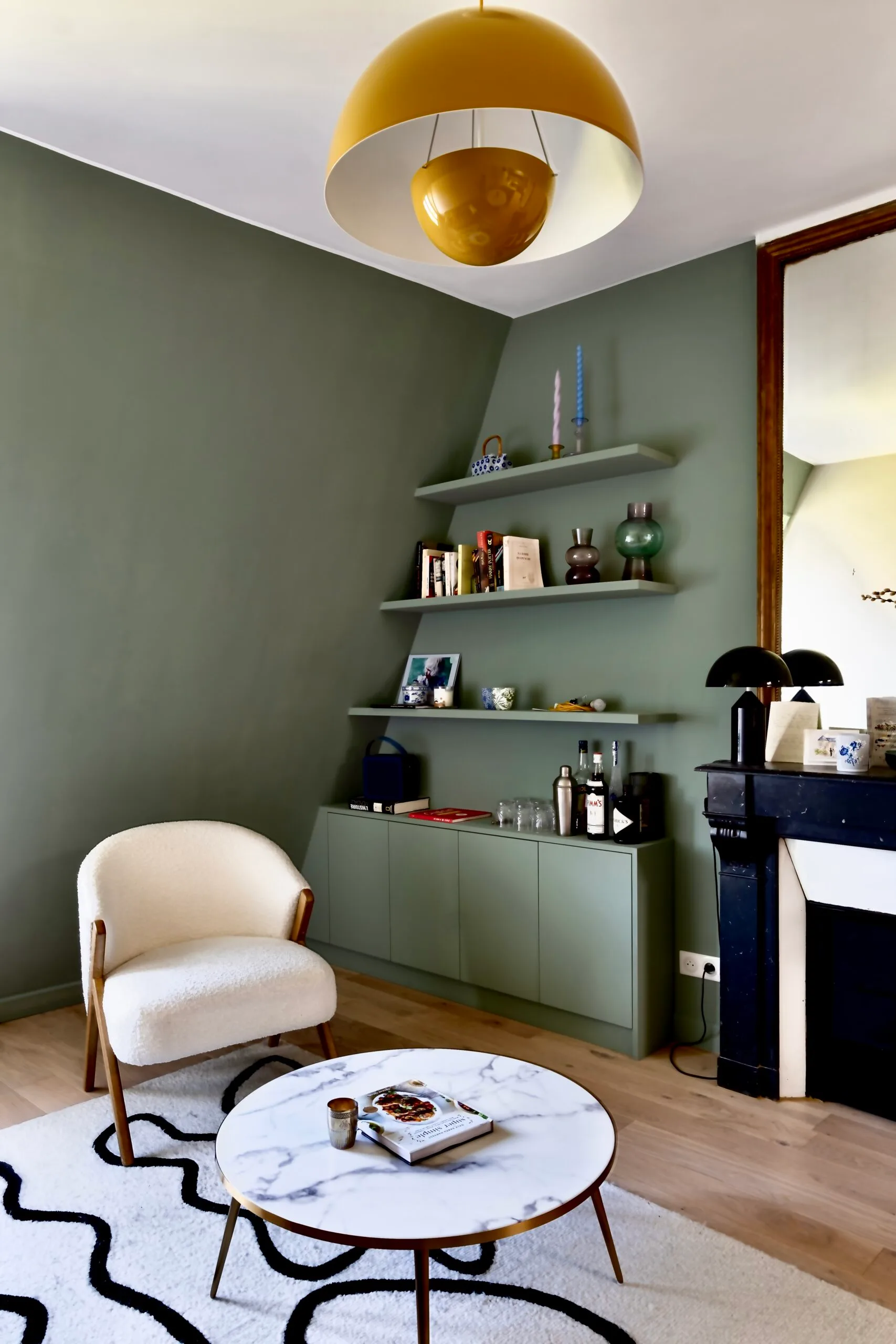 Coin bibliothèque vert sauge avec fauteuil bouclette et table basse design – combles rénovés Paris 17