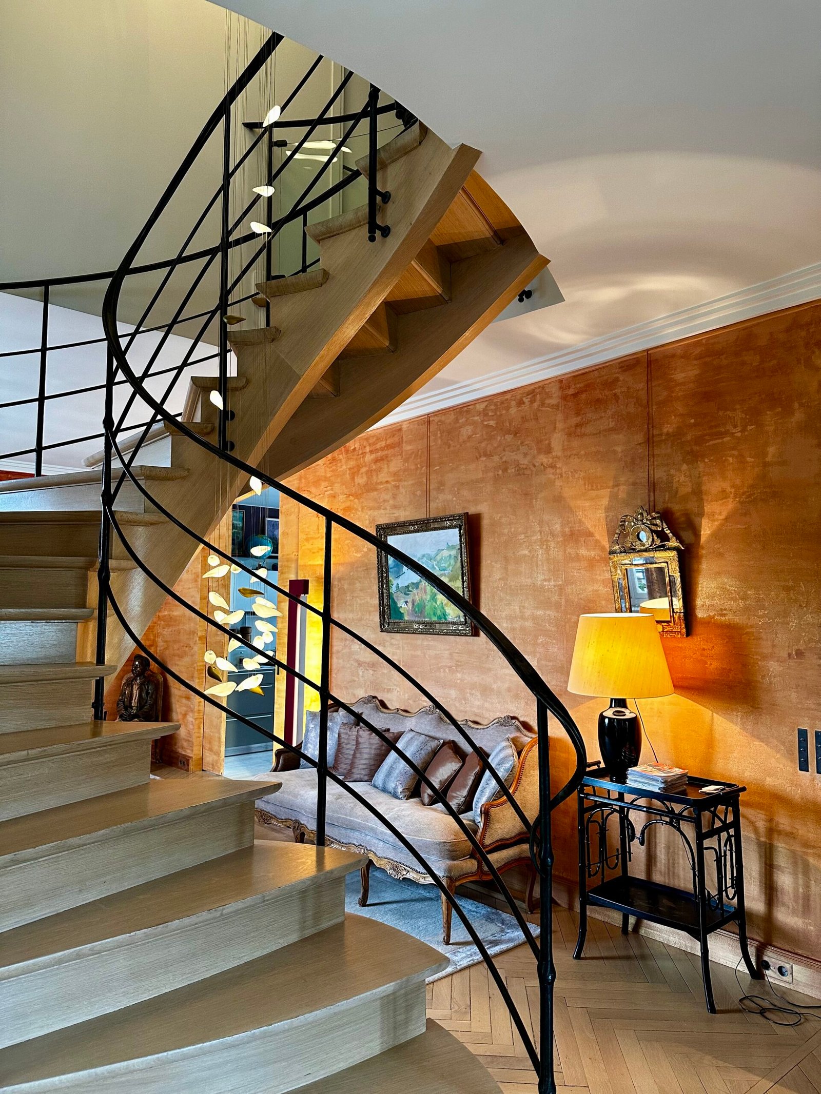 Escalier hélicoïdal mis en lumière par une suspension d'art – duplex haussmannien Paris 7