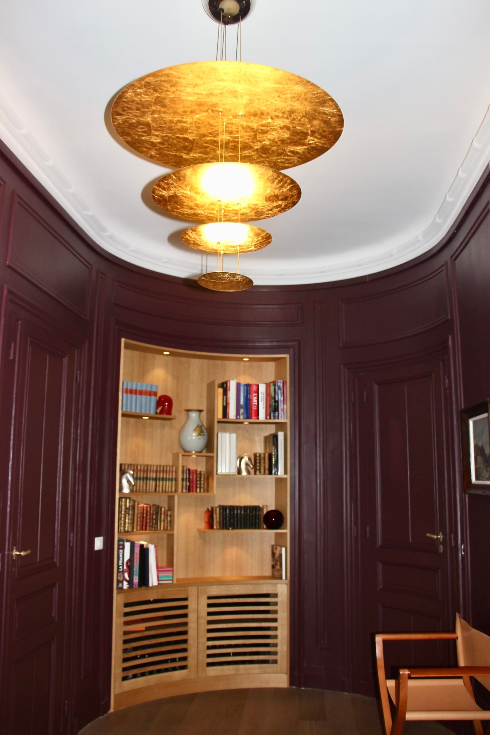 Luminaire en feuille d'or mettant en valeur le coloris aubergine de l'entrée de cet appartement haussmannien
