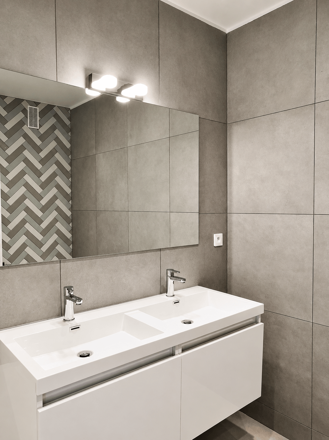Salle de bain rénovée à Paris 16 : meuble double vasque blanc, grandes dalles effet béton et briquettes en chevrons