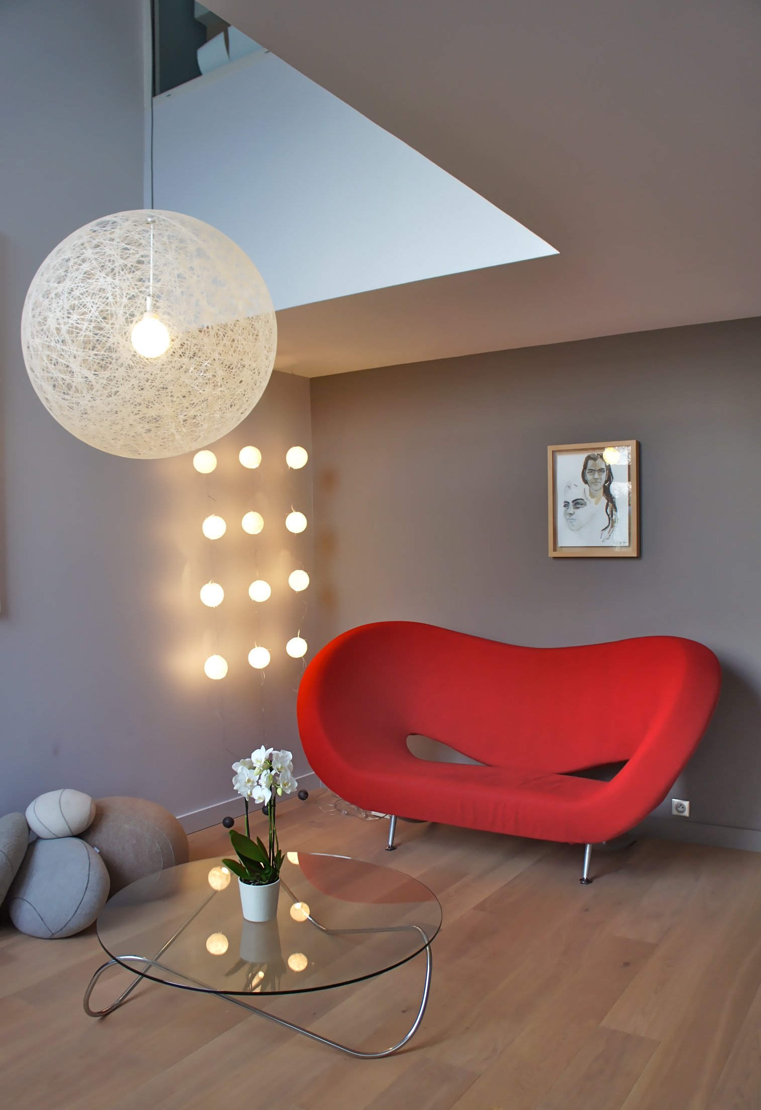 Salon avec canapé rouge design, suspension boule et parquet clair – appartement familial Paris 13